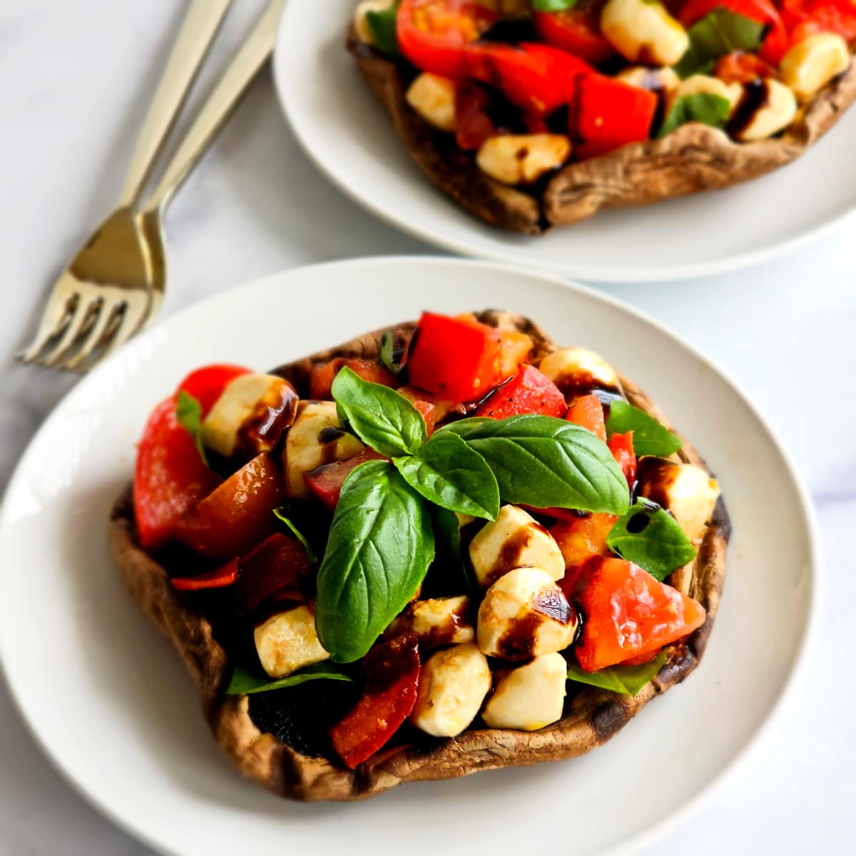 Grilled Portabella Caprese has 2 white plates piled with colorful salad, with 2 forks in a pile alongside.