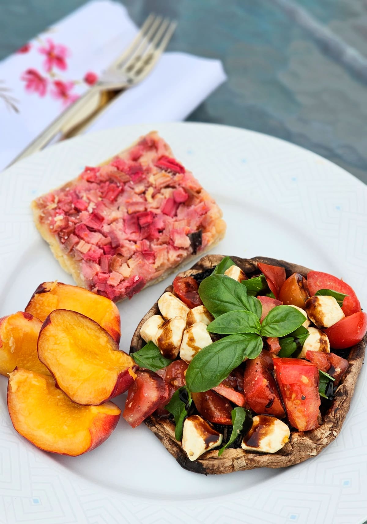 Grilled Portabella Caprese for lunch on a white plate with a peach and dessert on the plate, and a fork and napkin in the background.