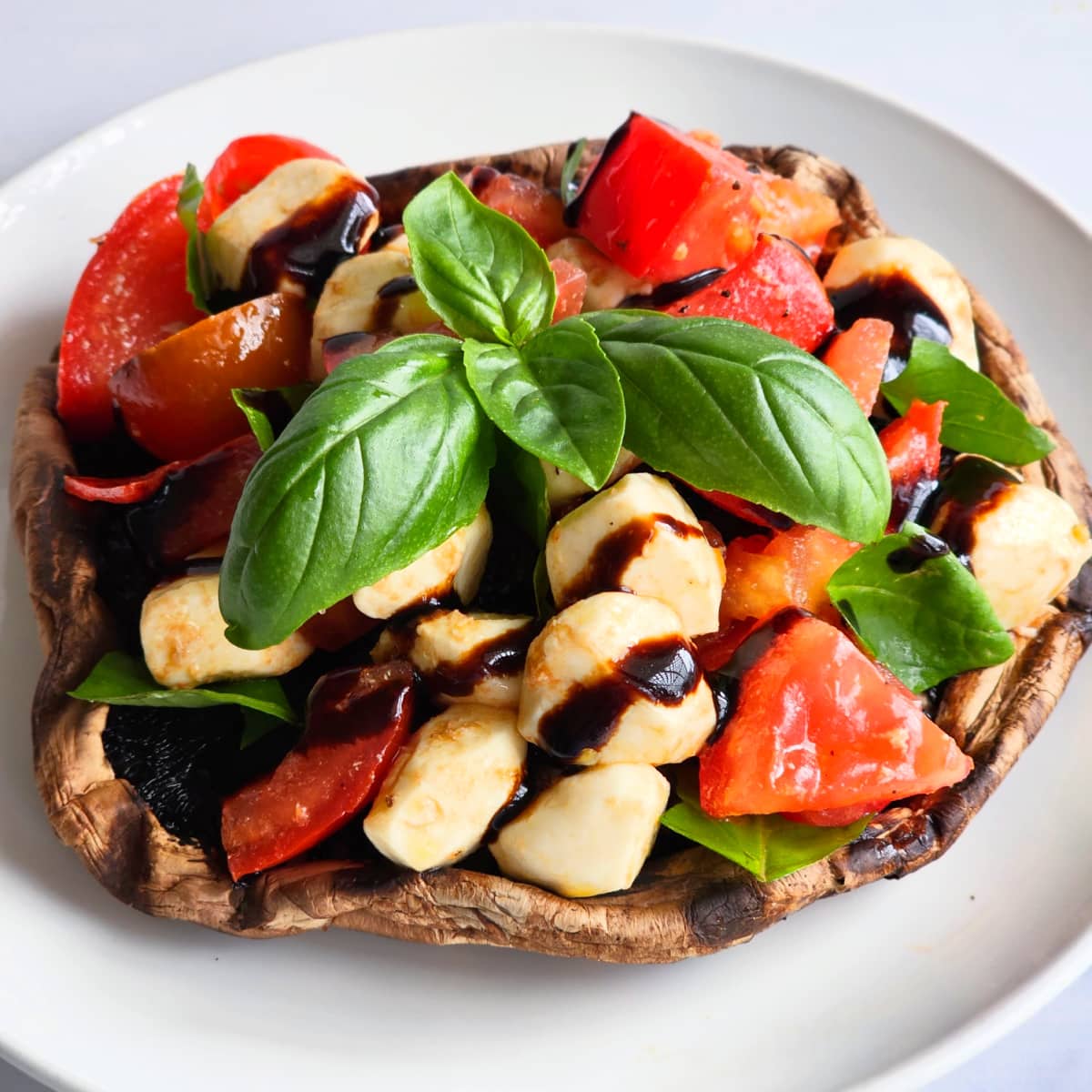 Colorful tomato mozzarella basil salad is piled atop a Portabella mushroom cap, resting on a white plate