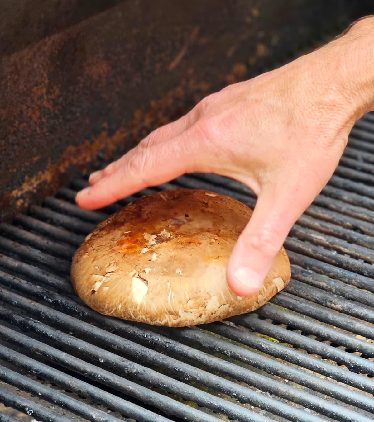 A hand places a Portabella mushroom on the grill for a Grilled Portabella Caprese
