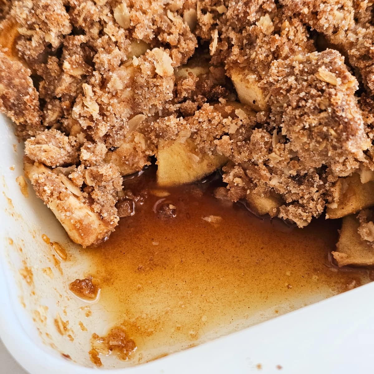 White baking dish with apple crisp, showing a portion removed 