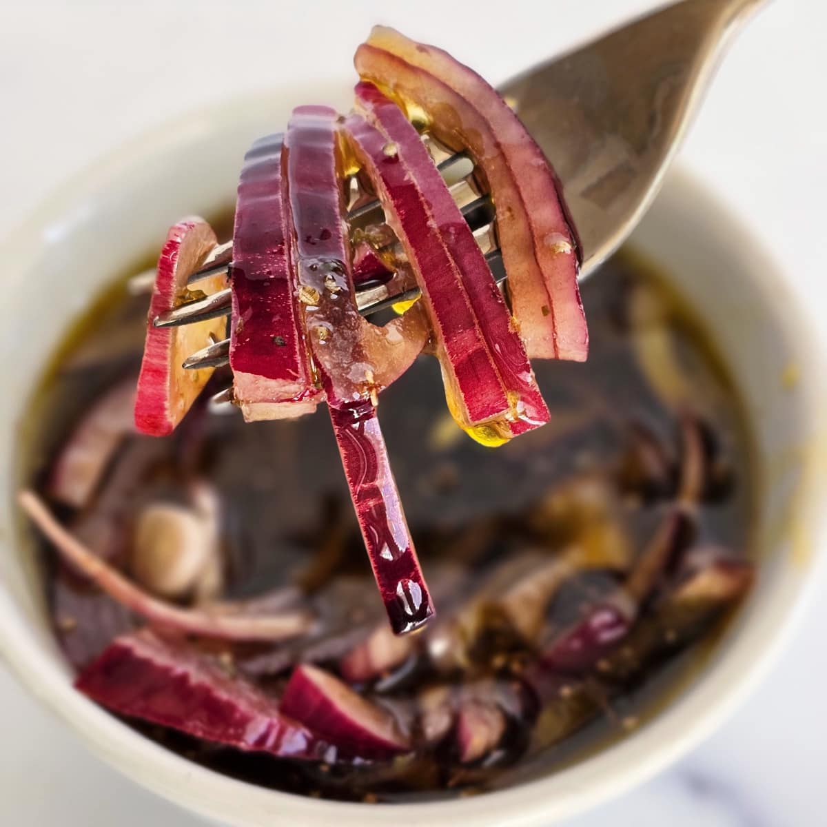 A fork lifts sliced red onions from a white bowl full of cut onions and marinade