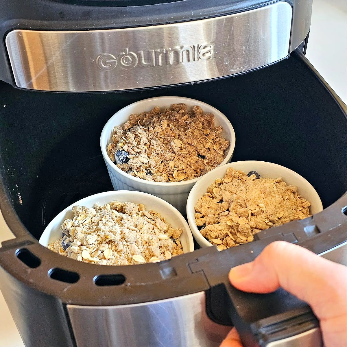 3 Blueberry Crisps in white ramekins in the black basket of an air fryer