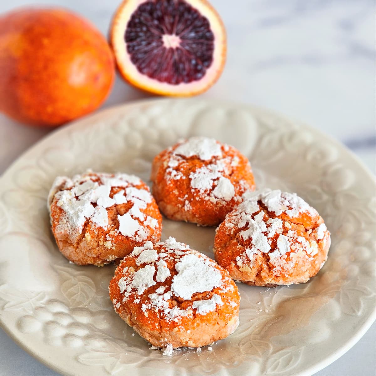 4 Blood Orange Crinkle Cookies on a white embossed plate on a white marble countertop