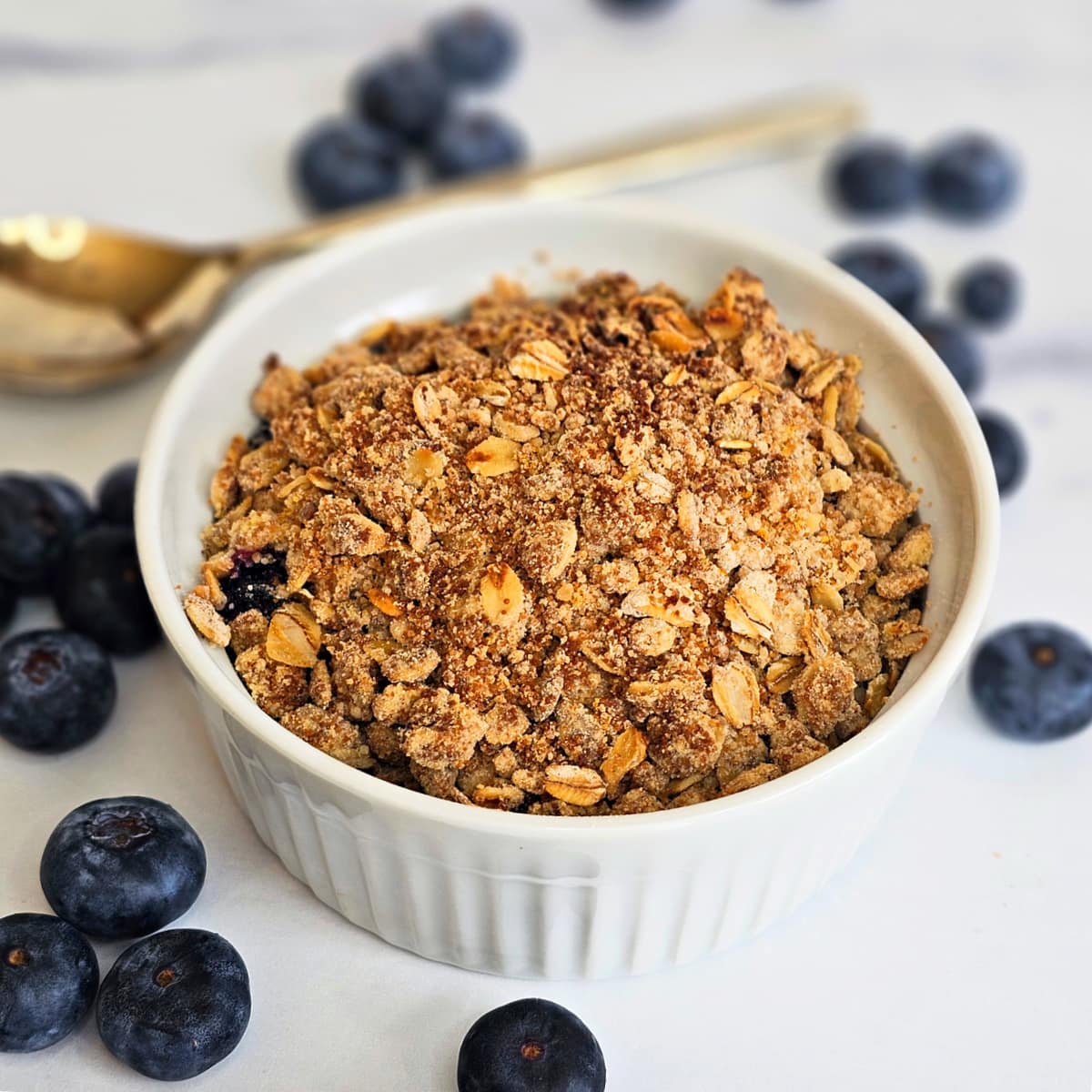 Air Fryer Blueberry Crisp in a white ramekin with fresh blueberries around it on the counter