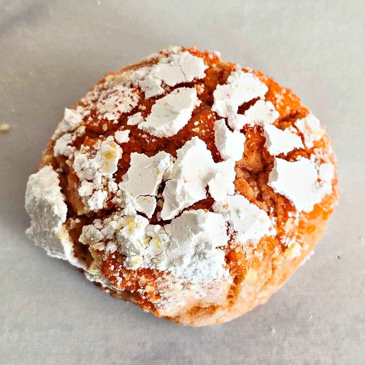 A blood orange crinkle cookie with cracked powdered sugar on the outside, on parchment paper