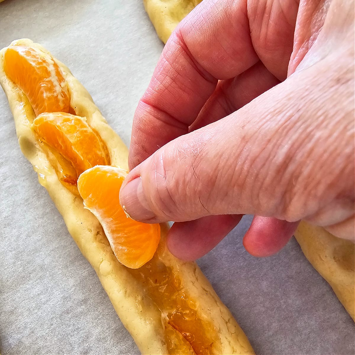 Fingers apply tangerine segments to the trough in a log of cookie dough