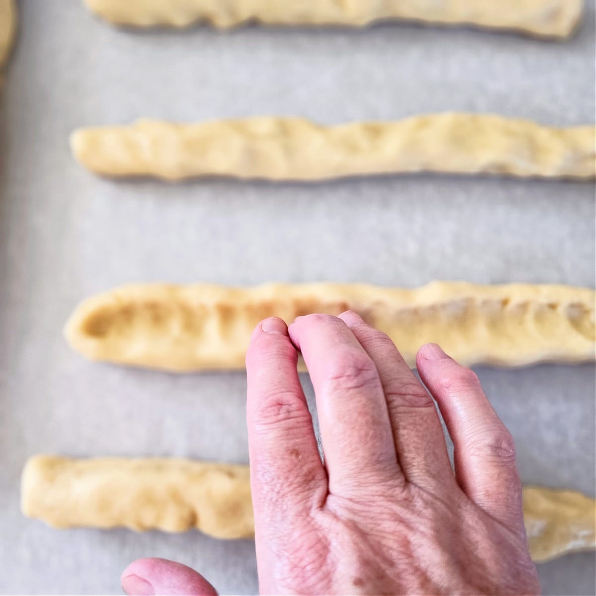 Fingers poised above dough logs to form troughs