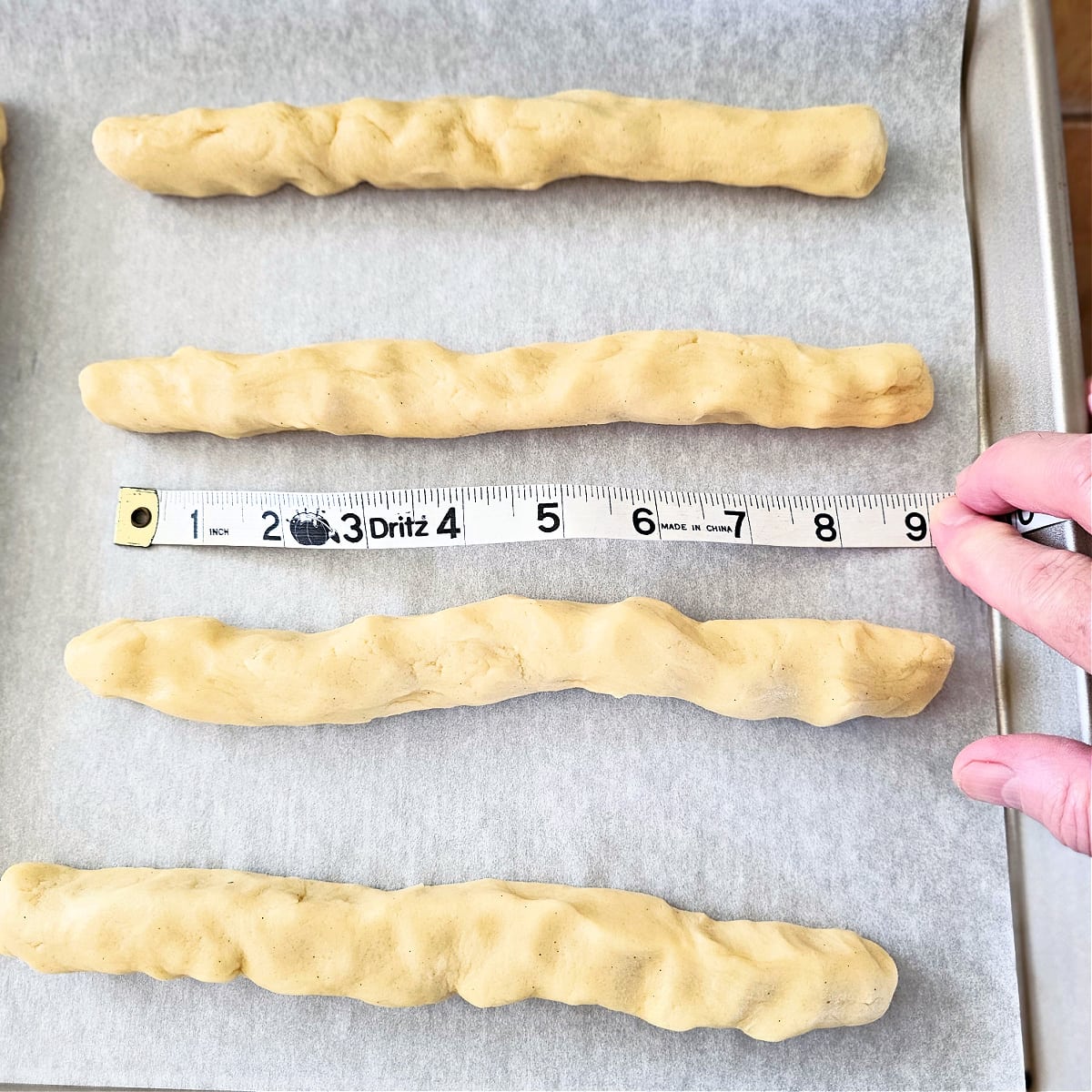 Fingers hold a measuring tape showing 9 inches for the cookie dough logs for Split Seconds Cookies