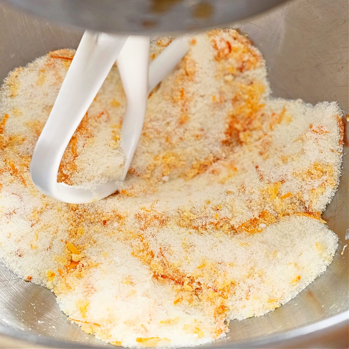 White mixing paddle mixes sugar and blood orange zest in a stainless steel mixing bowl