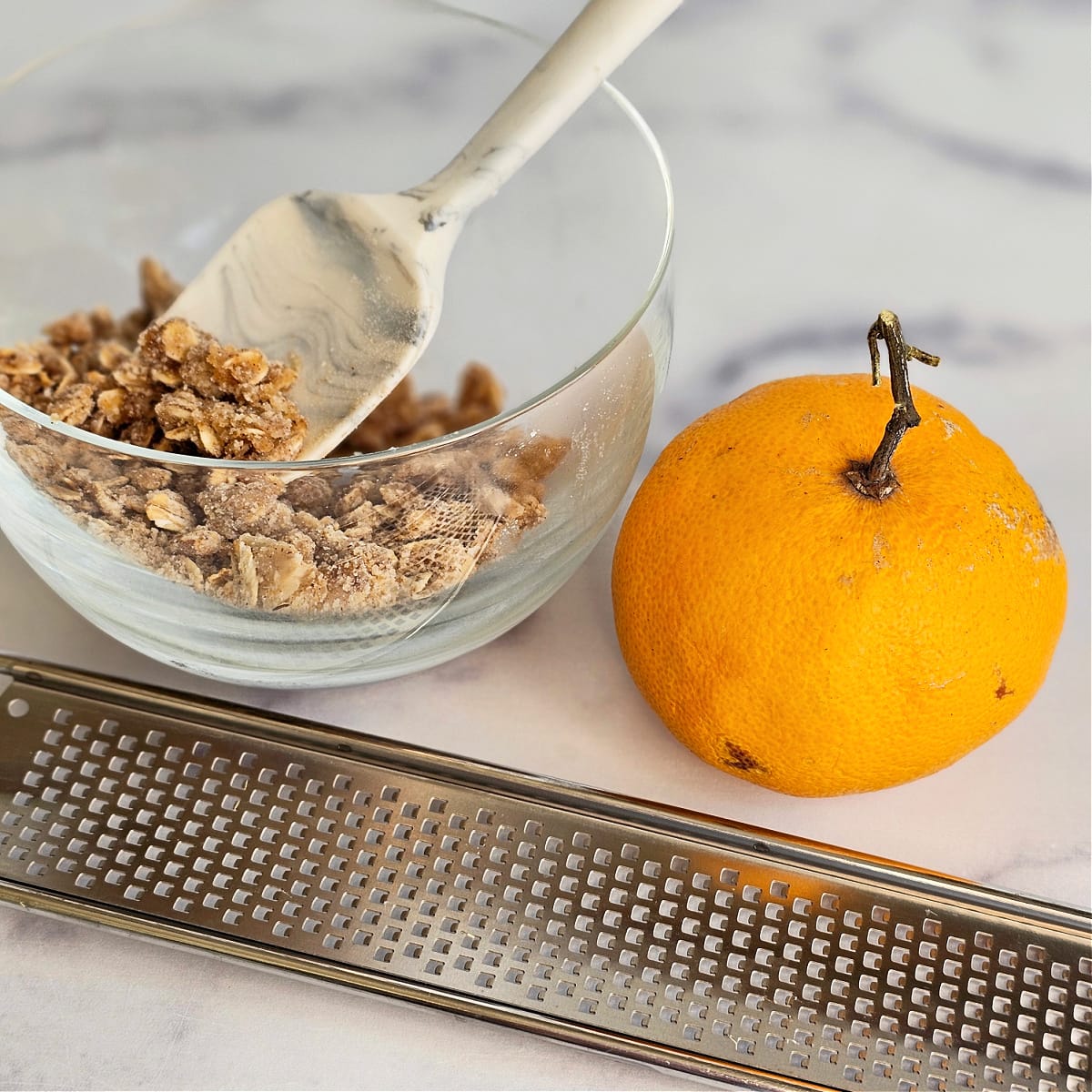 Whole orange and microplane tool sit on the counter with a bowl of crumb topping