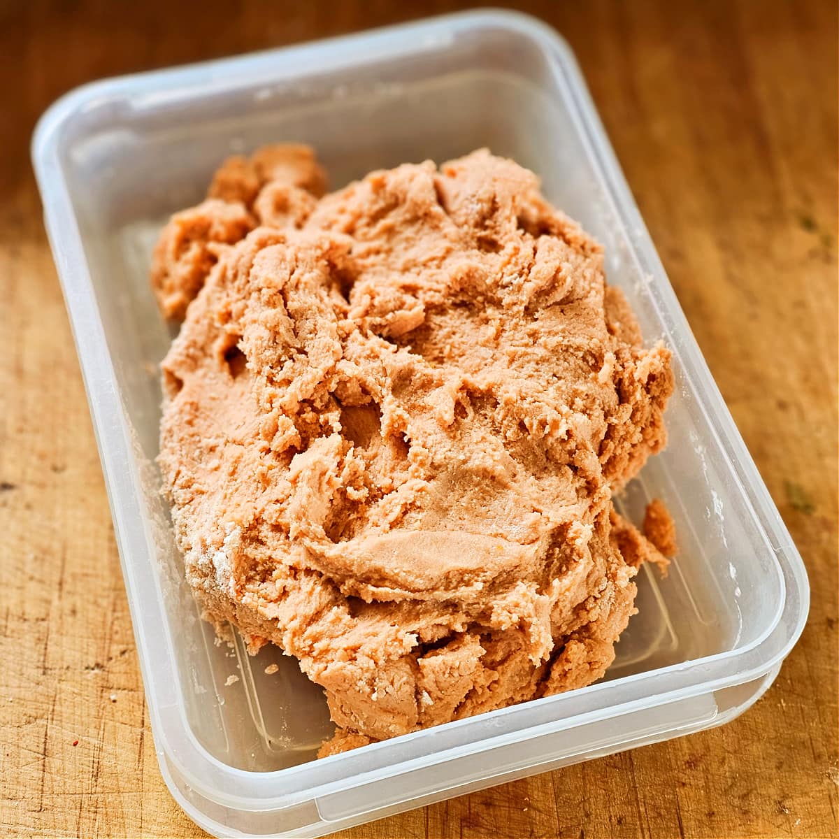 Orange cookie dough in a plastic rectangle container sitting on a wooden cutting board