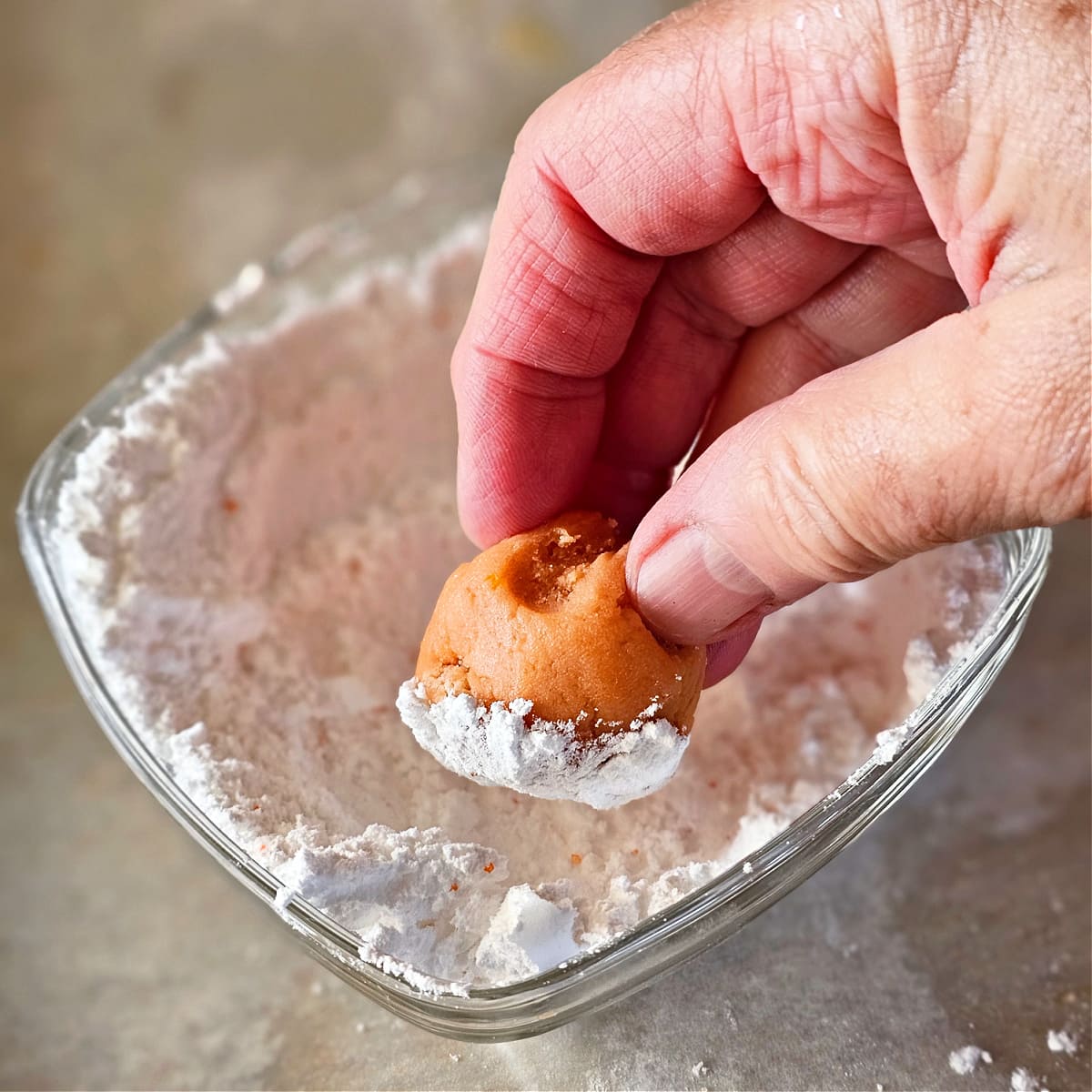 Hand rolls an orange cookie dough ball into powdered sugar