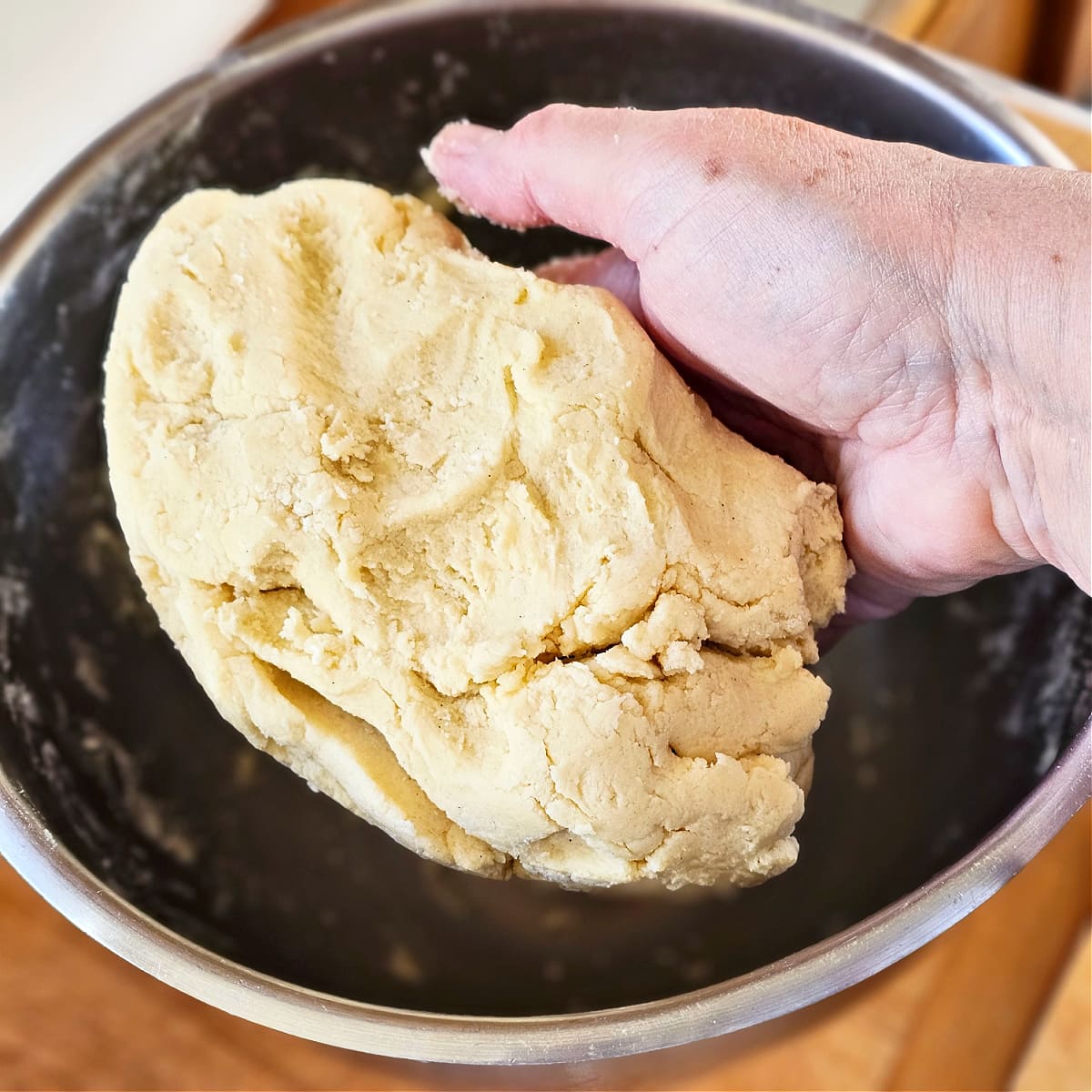 A hand holds Split Seconds Cookie dough above a stainless steel mixing bowl