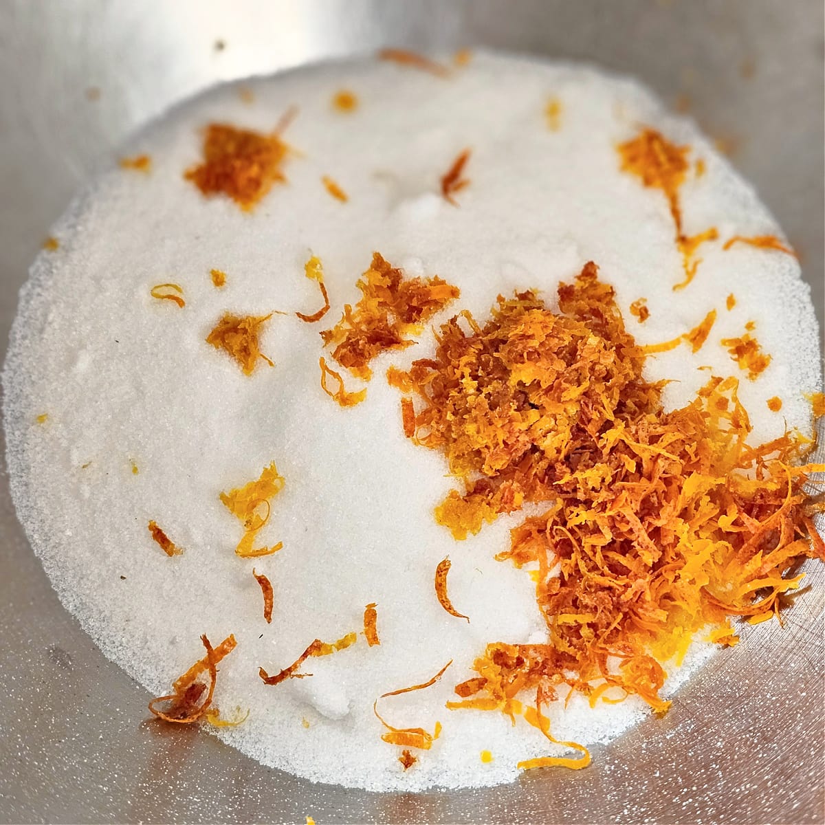 Sugar and blood orange zest in a stainless steel mixing bowl. 