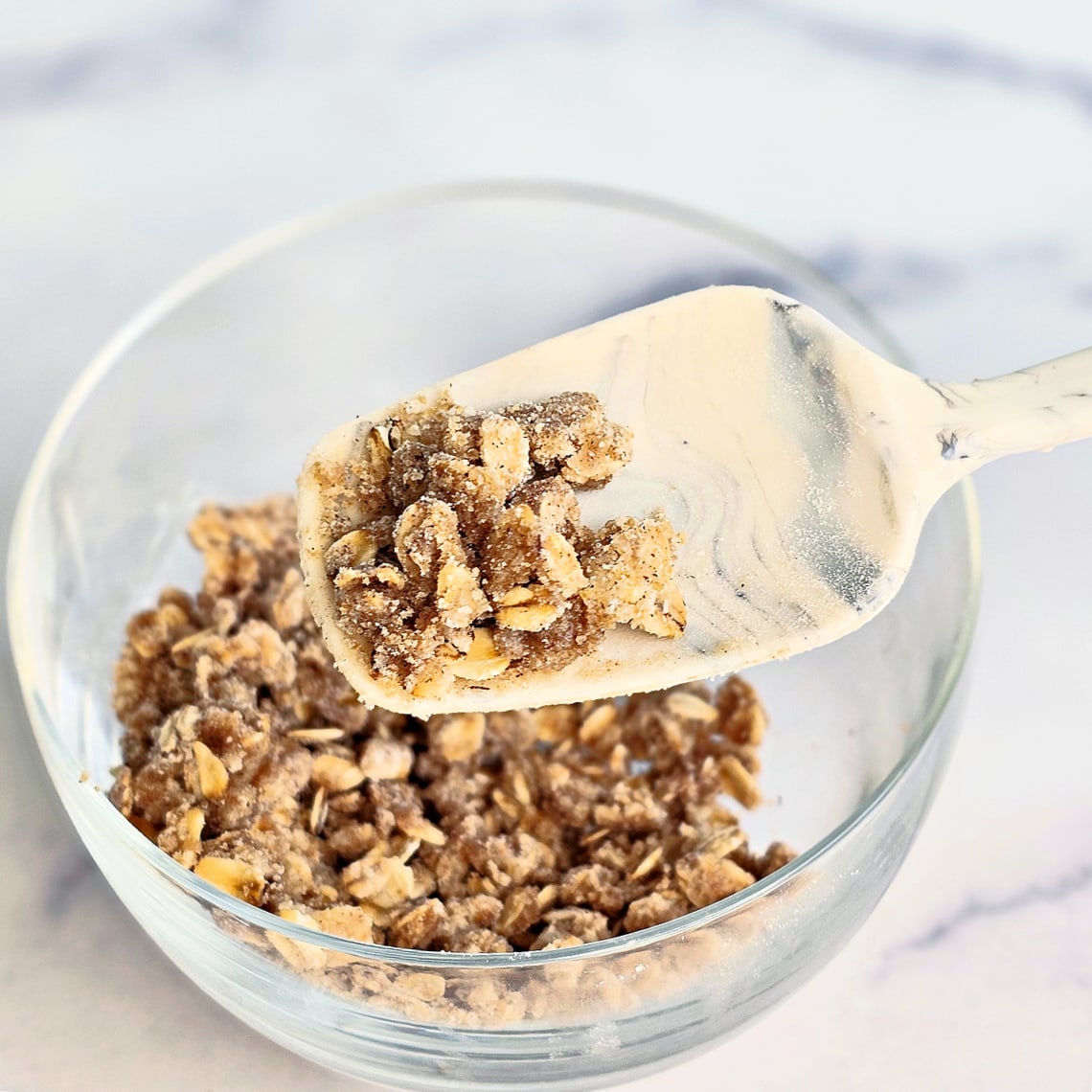 Topping for Air Fryer Blueberry Crisp in a clear glass bowl with a white spatula holding some up