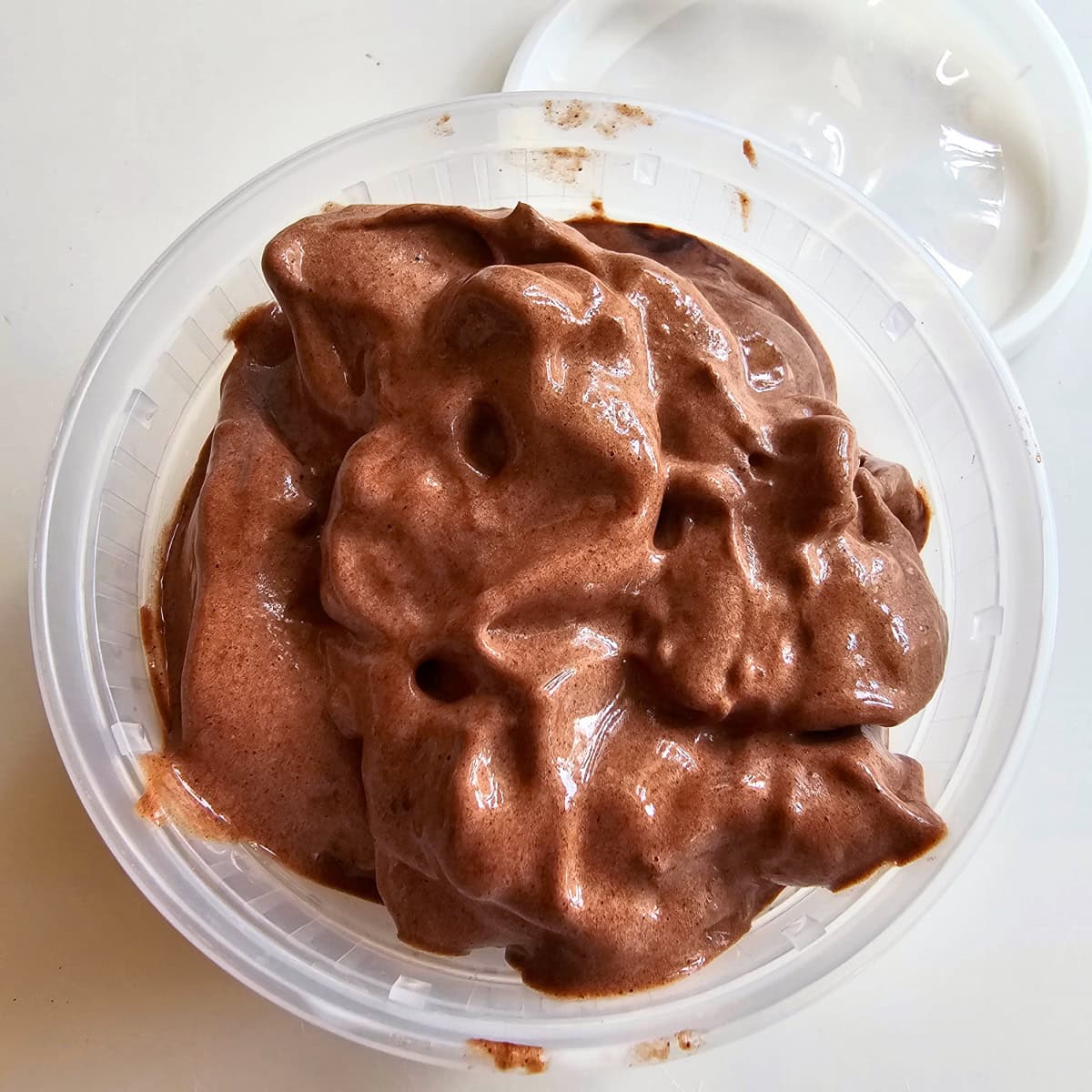Brown, shiny Vegan Chocolate Nice Cream in a plastic deli container on a white counter