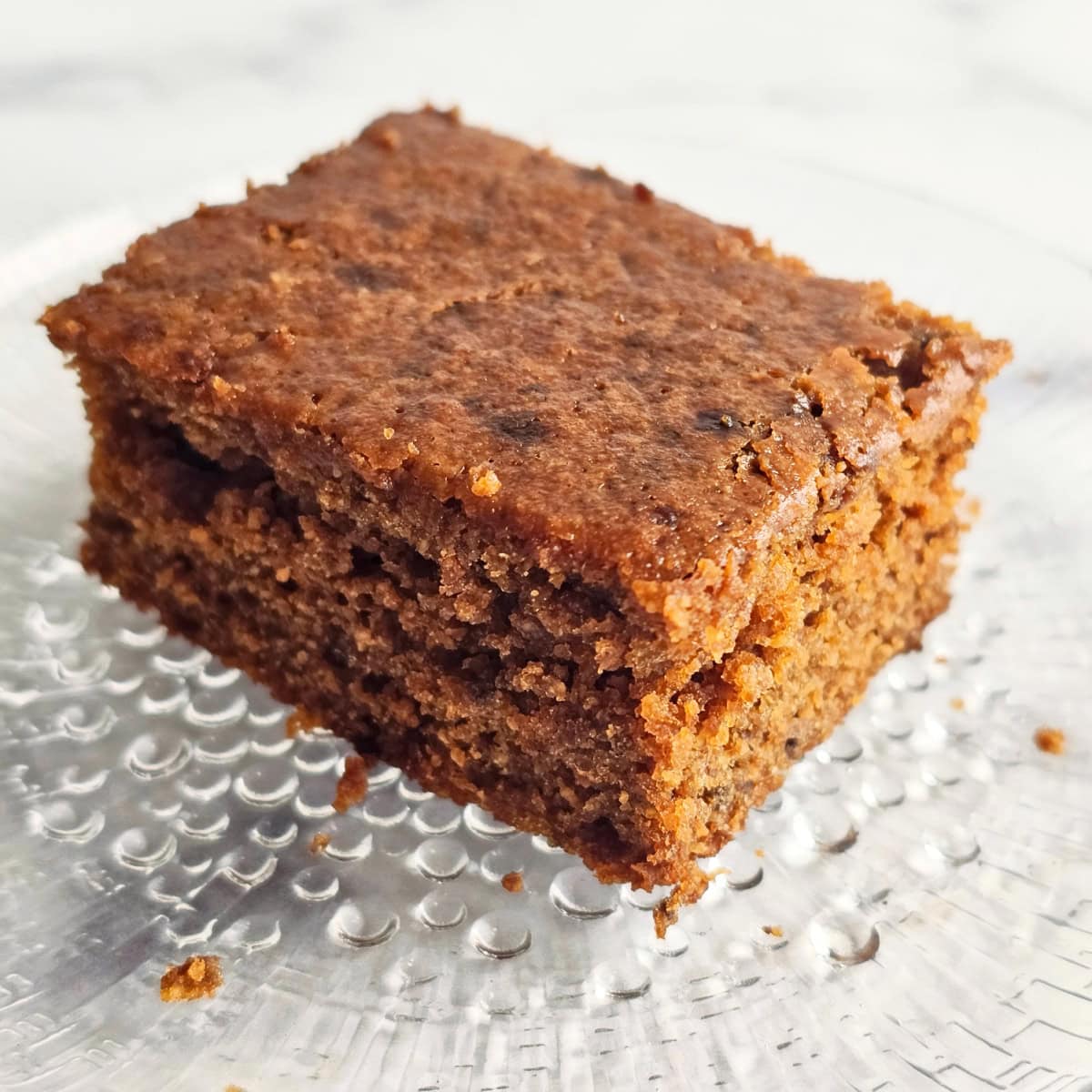 Brown colored Molasses Cornbread on a glass textured plate on a white marble countertop