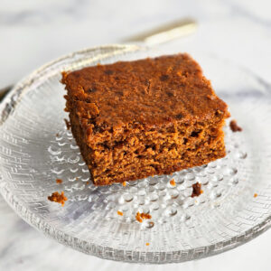 Square piece of brown Molasses Cornbread on a glass plate on a white marble countertop
