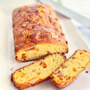 Loaf of Candied Ginger Cornbread with 2 slices cut off the end, on a white serving platter, with a knife perched on the right top end