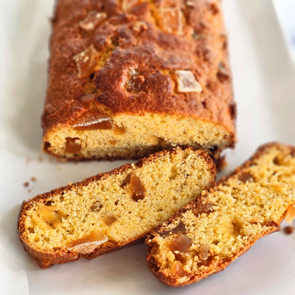 Loaf of Candied Ginger Cornbread with 2 slices cut and laid flat on the front end, on a rectangular white platter